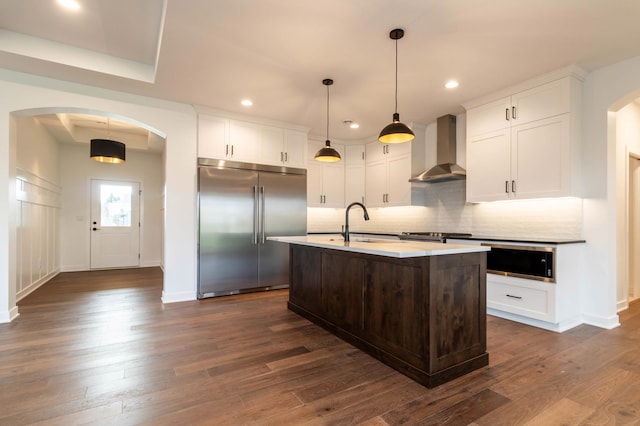 kitchen featuring wall chimney exhaust hood, built in fridge, and dark wood-type flooring