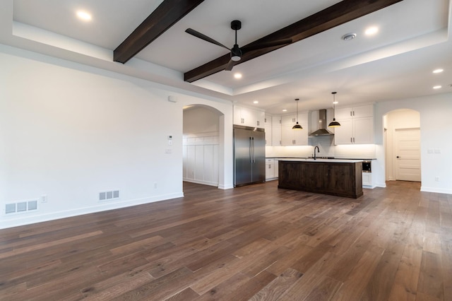 kitchen featuring high quality fridge, wall chimney exhaust hood, decorative light fixtures, a kitchen island with sink, and dark hardwood / wood-style flooring