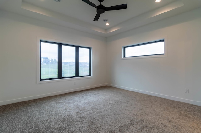 carpeted empty room with ceiling fan, a tray ceiling, and a healthy amount of sunlight