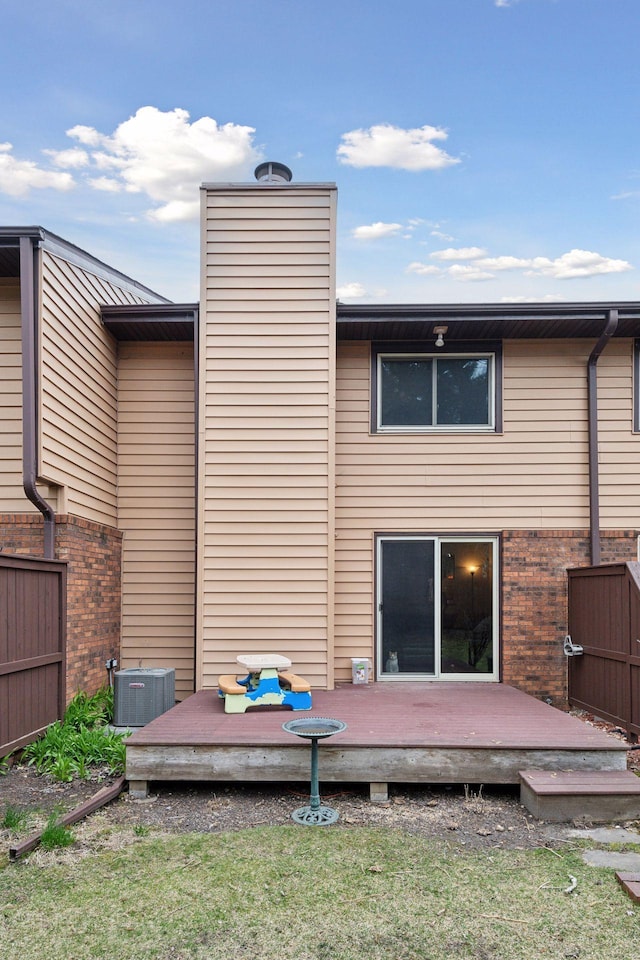 rear view of house with cooling unit, a deck, and a lawn