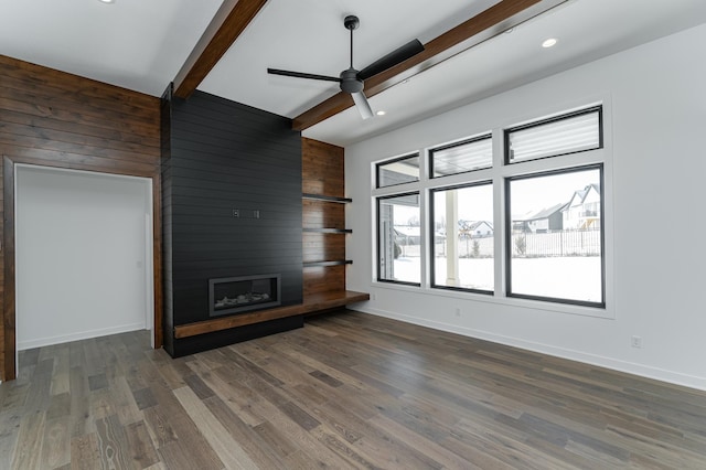 unfurnished living room featuring a fireplace, wood walls, beamed ceiling, ceiling fan, and dark wood-type flooring