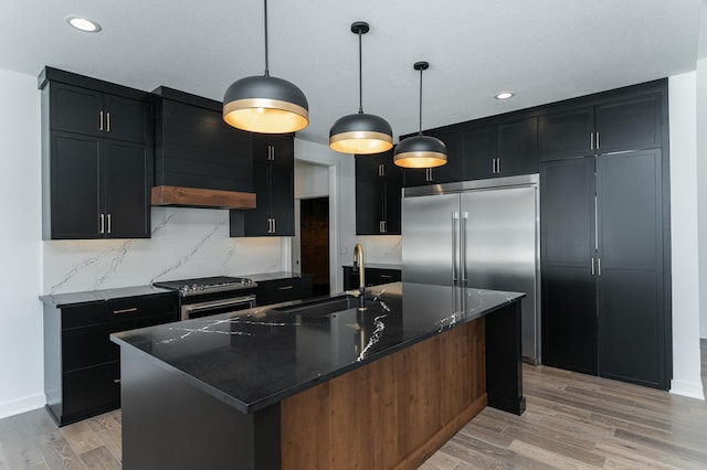 kitchen with pendant lighting, sink, dark stone counters, and a center island with sink