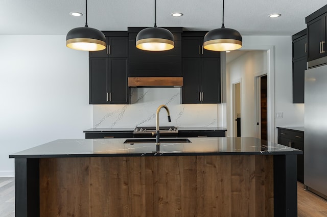 kitchen with backsplash, decorative light fixtures, stainless steel fridge, and an island with sink