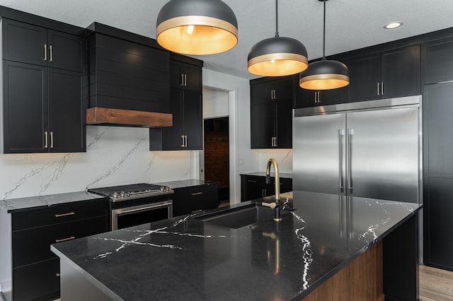 kitchen featuring sink, stainless steel appliances, dark stone counters, and a large island with sink