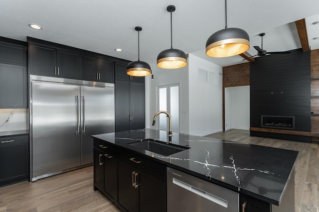 kitchen featuring decorative light fixtures, an island with sink, sink, dark stone countertops, and stainless steel appliances