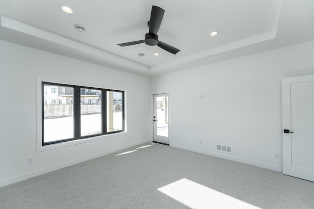 empty room featuring light carpet, ceiling fan, and a tray ceiling