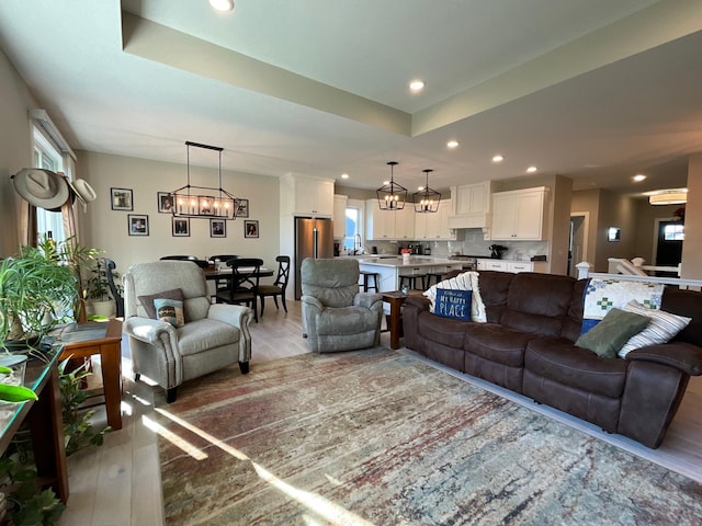 living room featuring a chandelier, light hardwood / wood-style floors, a raised ceiling, and sink