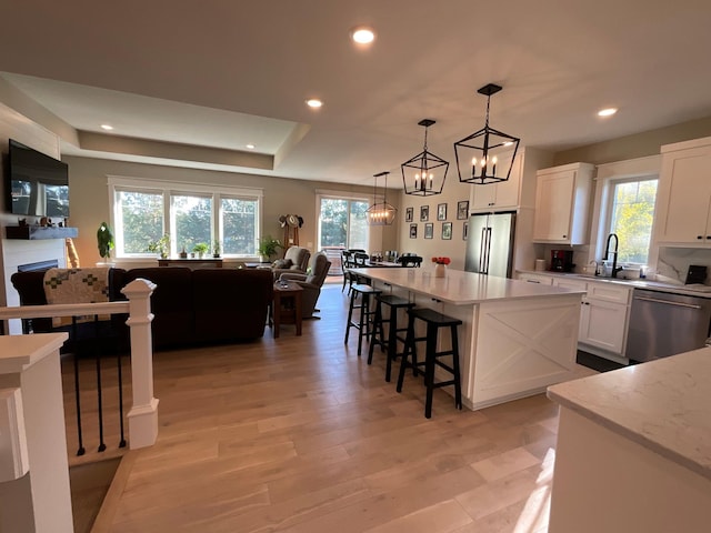 kitchen featuring decorative light fixtures, stainless steel appliances, light wood-type flooring, and white cabinetry