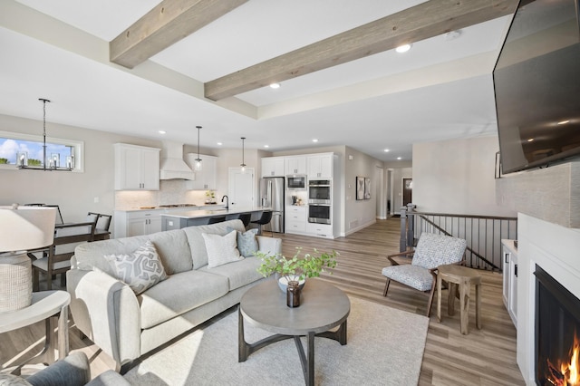 living room with an inviting chandelier, light wood-type flooring, sink, and beam ceiling