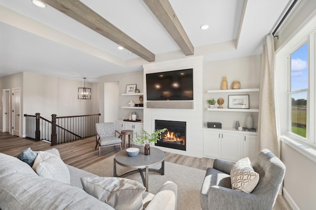 living room featuring light hardwood / wood-style floors, a large fireplace, beamed ceiling, and a notable chandelier