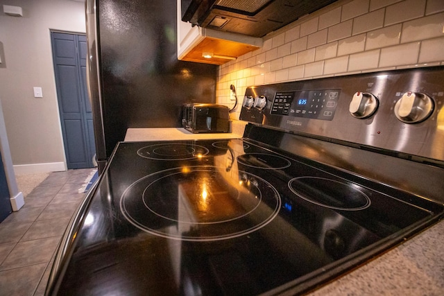 kitchen with backsplash, black / electric stove, and dark tile patterned flooring