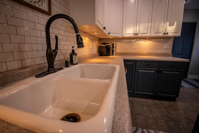 kitchen featuring white cabinetry, dark tile patterned flooring, light stone counters, backsplash, and sink