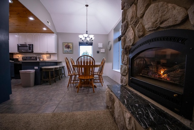 dining room featuring an inviting chandelier, dark tile patterned flooring, lofted ceiling, and a fireplace