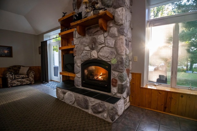 tiled living room with wooden walls, a stone fireplace, vaulted ceiling, and a wealth of natural light