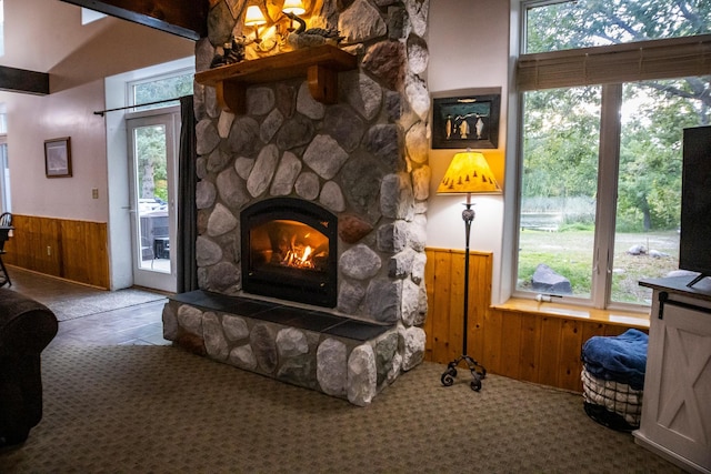 carpeted living room with wooden walls, a healthy amount of sunlight, and a stone fireplace