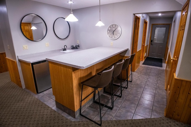 kitchen with hanging light fixtures, dark tile patterned flooring, kitchen peninsula, a breakfast bar area, and sink