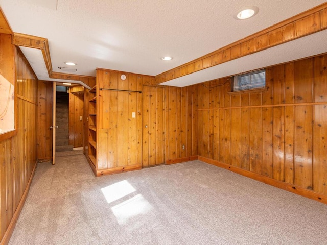 carpeted empty room featuring a textured ceiling and wooden walls