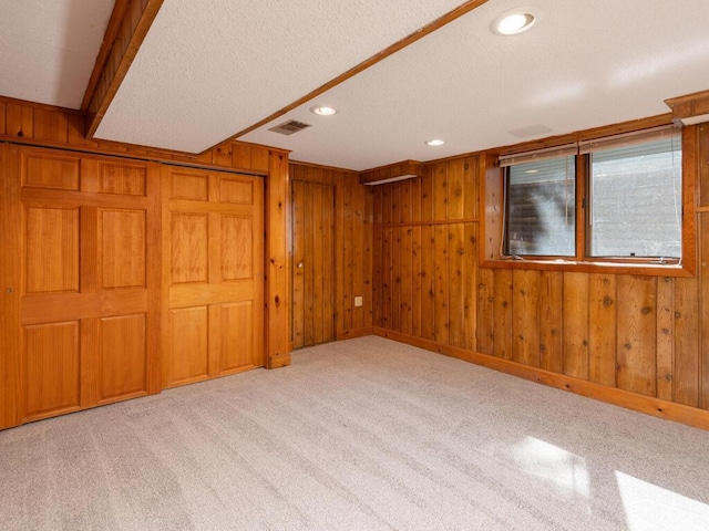 interior space featuring a textured ceiling, light colored carpet, and wooden walls