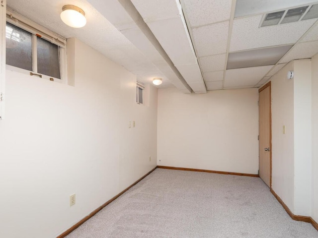 basement featuring a drop ceiling and light colored carpet