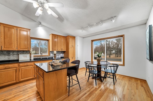 kitchen featuring lofted ceiling, backsplash, a sink, light wood-type flooring, and a kitchen bar