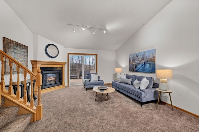 carpeted living room featuring a textured ceiling, baseboards, vaulted ceiling, stairway, and a glass covered fireplace