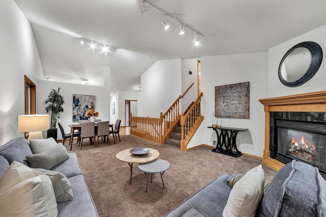 carpeted living room with a fireplace, lofted ceiling, rail lighting, baseboards, and stairs