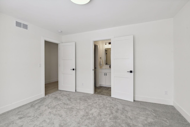 unfurnished bedroom with ensuite bath and light colored carpet