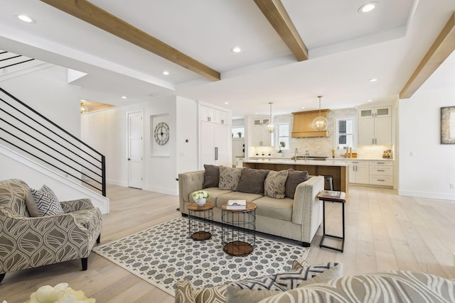 living room featuring beamed ceiling, sink, light hardwood / wood-style floors, and a healthy amount of sunlight