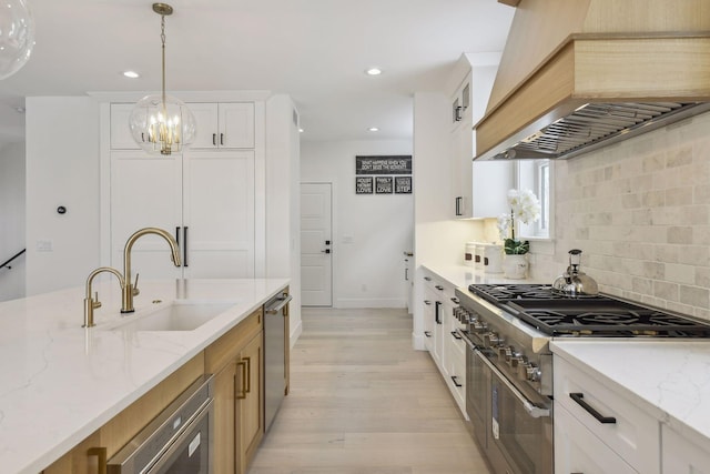 kitchen with white cabinets, premium range hood, sink, appliances with stainless steel finishes, and light stone countertops