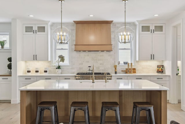 kitchen with custom range hood, an island with sink, and white cabinets