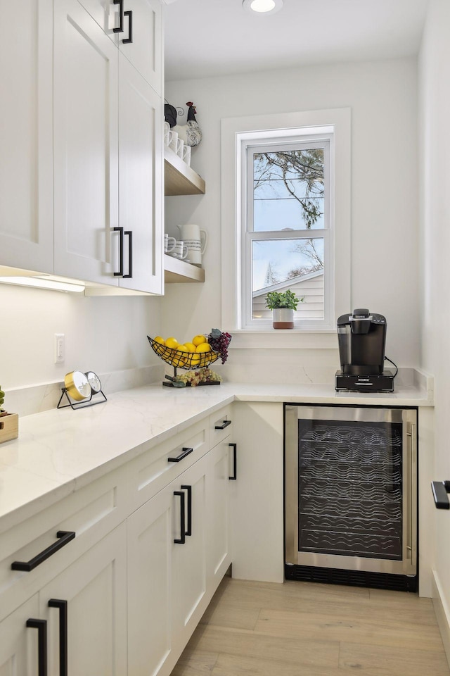 bar with white cabinets, wine cooler, light stone countertops, and light hardwood / wood-style floors