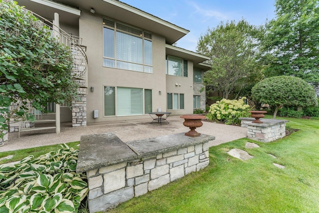 back of property featuring a patio area, stone siding, a yard, and stucco siding