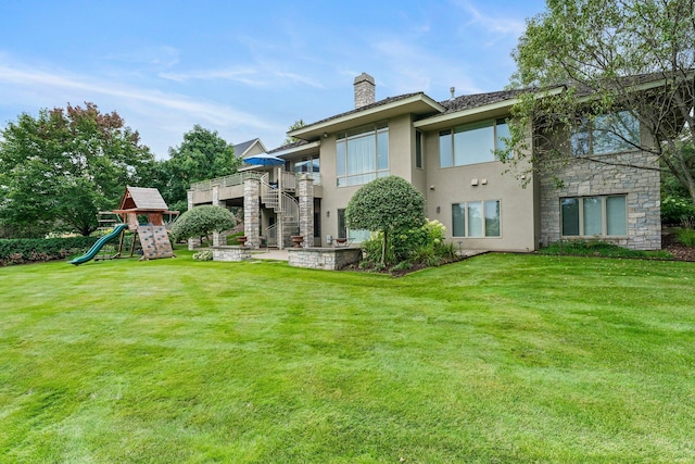 rear view of property featuring stone siding, a lawn, a chimney, a playground, and stucco siding