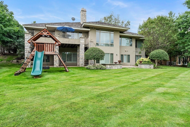 rear view of house featuring stucco siding, a chimney, stone siding, a yard, and a playground