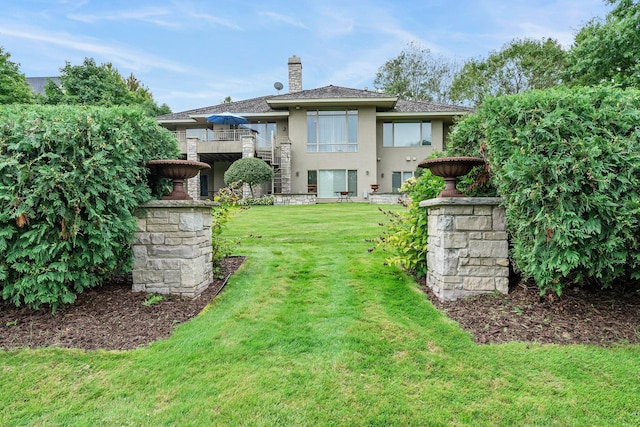 back of property featuring stucco siding, a chimney, stairway, stone siding, and a yard