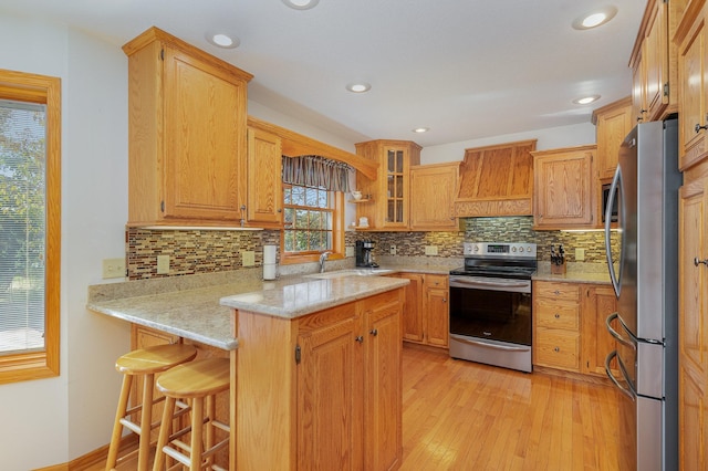 kitchen featuring custom exhaust hood, backsplash, appliances with stainless steel finishes, a breakfast bar, and light hardwood / wood-style flooring