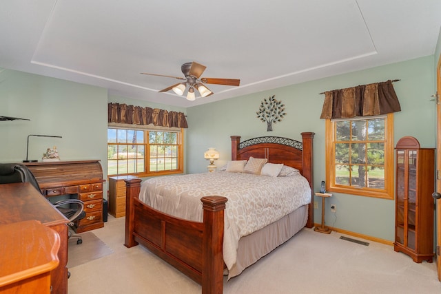 bedroom with ceiling fan, light carpet, and a tray ceiling