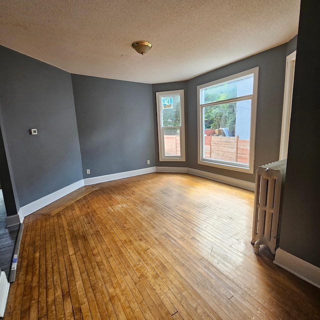 empty room with light wood-type flooring, a textured ceiling, and radiator heating unit