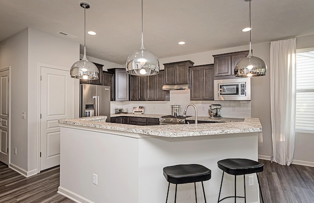 kitchen with pendant lighting, a kitchen island with sink, appliances with stainless steel finishes, dark hardwood / wood-style flooring, and dark brown cabinetry