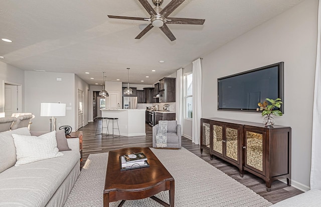 living room with a textured ceiling, ceiling fan, and dark wood-type flooring