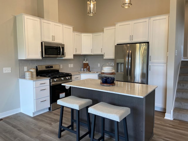 kitchen with white cabinetry, a kitchen island, pendant lighting, stainless steel appliances, and wood-type flooring