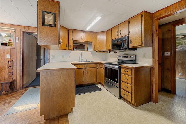 kitchen featuring stainless steel electric stove, wood walls, and sink