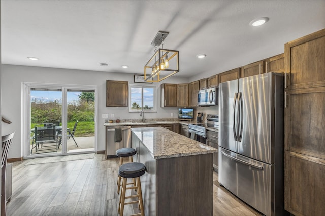 kitchen with pendant lighting, sink, stainless steel appliances, light stone countertops, and a kitchen island