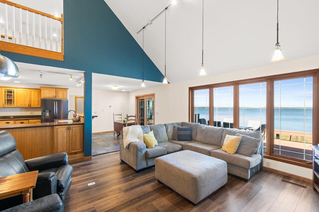 living room with track lighting, sink, high vaulted ceiling, a water view, and dark hardwood / wood-style flooring