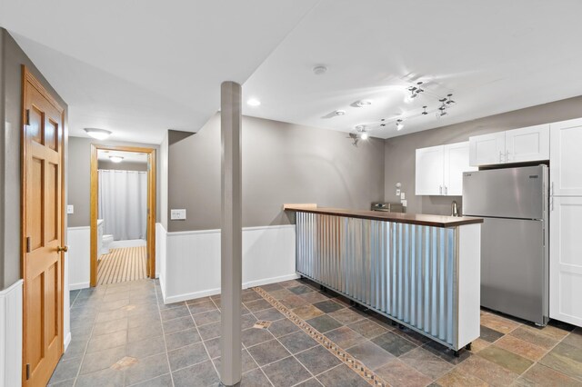 kitchen with stainless steel refrigerator, kitchen peninsula, and white cabinetry