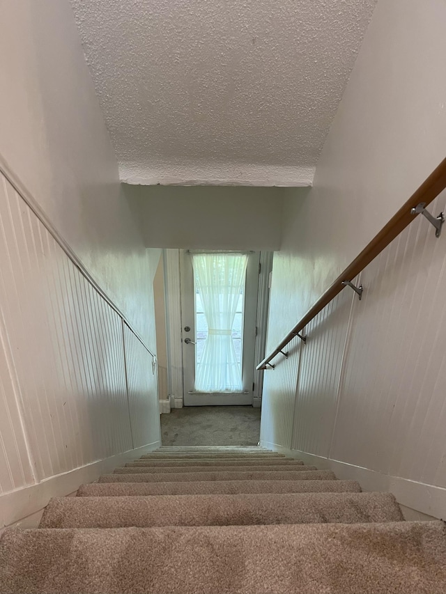 stairs with a textured ceiling and carpet flooring