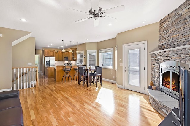 dining area featuring baseboards, ceiling fan, a stone fireplace, recessed lighting, and light wood-style flooring