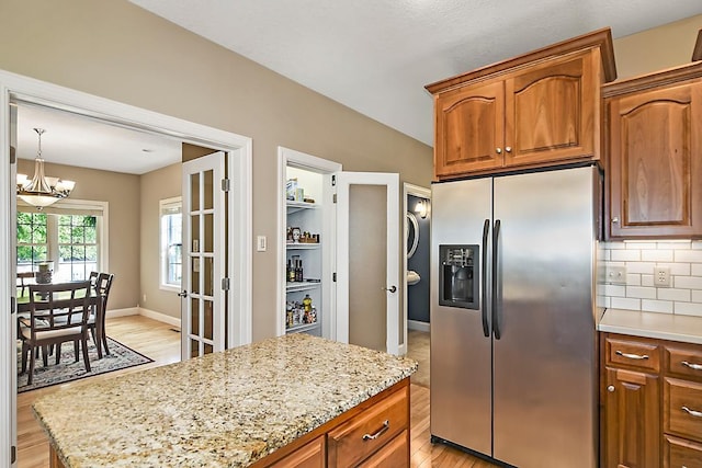 kitchen with brown cabinets, stainless steel refrigerator with ice dispenser, light wood finished floors, decorative backsplash, and light stone countertops