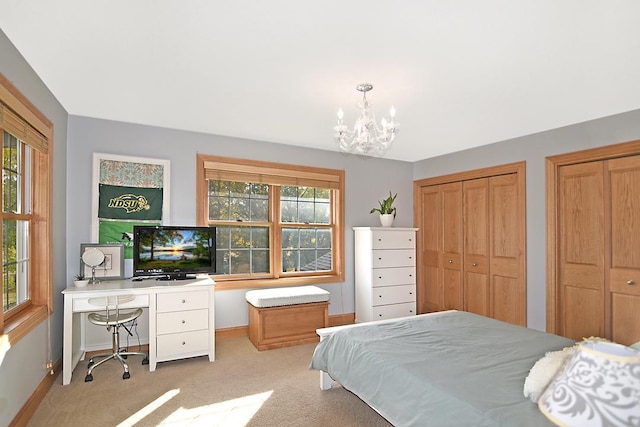 carpeted bedroom featuring baseboards, multiple windows, two closets, and an inviting chandelier