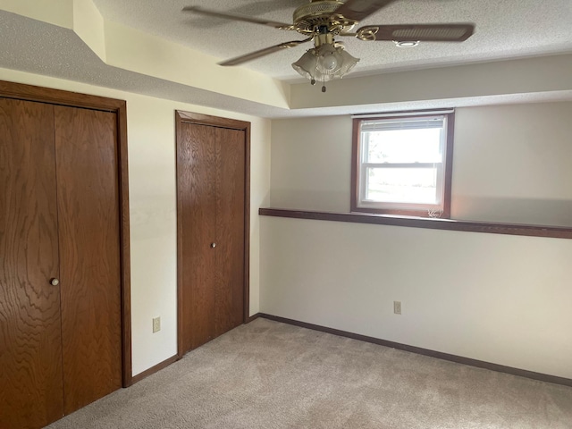 unfurnished bedroom with a textured ceiling, two closets, ceiling fan, and light colored carpet